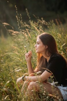 Summer photo of a girl on the background of a grass meadow.. The beauty sits in the summer among the grass in the meadow 3659.