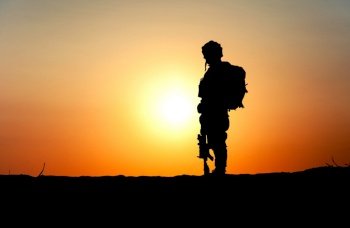 Silhouette of army infantry in tactical ammunition and backpack on back, standing in desert with service rifle on ground with bright sunset on background. Missing in action, fallen in battle soldier. Army soldier silhouette on rising sun background