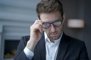 Close up of concentrated handsome austrian businessman dressed in suit adjusting glasses while working in office, executive man in spectacles at workplace. Business people concept. Concentrated handsome austrian businessman dressed in suit adjusting glasses while working in office
