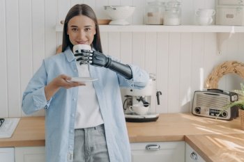 Happy disabled european woman is holding cup of coffee with cyber hand. Concept of grasp sensors in electronic high technology arm prosthesis. Routine of amputee person and life quality.. Happy disabled european woman is holding cup of coffee with cyber hand. Routine of amputee person.