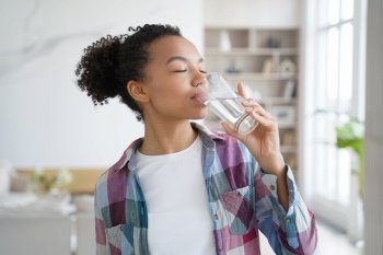 African american woman enjoy drinking pure crystal filtered potable water. Thirsty female with eyes closed swallow mineral aqua from glass at home kitchen. Thirst, healthy lifestyle, body care concept. African american young girl enjoy drinking pure filtered water from glass at home. Healthy lifestyle