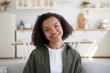 Portrait of happy afro girl at home. Young african american woman among modern scandinavian interior in her room. Trendy curly hairstyle, optimistic smile and attractive appearance. Positive emotions.. Portrait of happy afro girl at home. Curly hairstyle, optimistic smile and positive emotions.