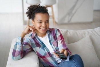 Smiling biracial teen girl sit rest on couch watch TV at home. Happy young woman relax on sofa enjoy television program online in living room on domestic weekend. Entertainment concept.. Smiling biracial young girl enjoy television program, watch TV series, sitting on couch at home
