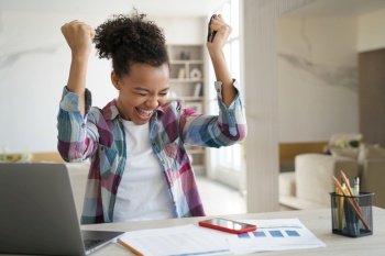 Excited african american teen girl received good news email on laptop, biracial high schoolgirl got good exam scores, clenching her fists making yes gesture celebrates win, personal success.. Excited african american teen girl received good news email on laptop screams, makes yes gesture