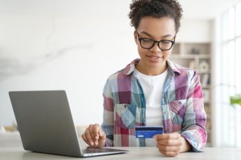 African american teen girl holds credit bank card shopping online on laptop. Young biracial female buy pay on internet on computer at home, browsing banking services, checking cashback bonus.. African american teen girl holds credit bank card uses banking services online on laptop. E-commerce