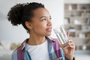 Lovely young hispanic woman enjoying mineral water at home. Positive afro teenage girl drinks water from a glass. Weight loss dieting, fitness and wellness. Healthy lifestyle choice concept.. Lovely young hispanic woman enjoying mineral water. Healthy lifestyle, fitness and wellness.