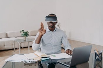 African american man businessperson uses virtual reality glasses with augmented reality technology sitting at laptop at office desk. Modern black guy working on project in cyberspace wears VR goggles. African american businessman using virtual reality glasses working at laptop. Hightech, e-business
