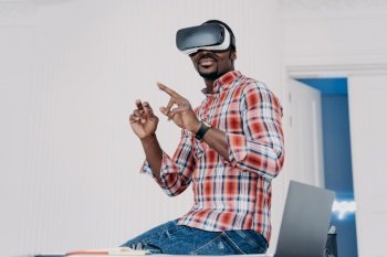 Happy african american guy in vr goggles at home. Young businessman has virtual study. Executive is working on futuristic design project. Modern digital gadget for business and e-learning.. Happy african american guy in vr goggles at home. Freelancer .working on futuristic design project.