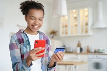 Happy hispanic young woman is purchasing online with mobile phone and credit card. Smiling teenage girl spends money from home. Online shopping, internet banking. Business and e-commerce.. Happy young woman is purchasing online with mobile phone and credit card. Internet banking.