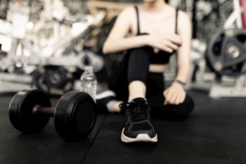 exercise concept The female with dark tone of outfits resting herself on the black carpet floor after playing on the dumbbell beside her.