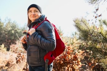 Happy woman enjoying hike on sunny vacation day. Female with backpack walking through forest. Spending summer vacation close to nature