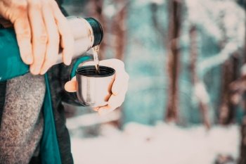 man pouring hot tea in winter forest