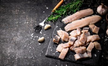 Pieces of salted herring on a stone board with garlic and rosemary. On a black background. High quality photo. Pieces of salted herring on a stone board with garlic and rosemary. 