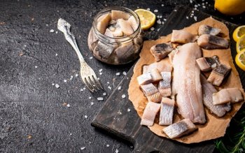 Fillet of salted herring on paper on a cutting board. On a black background. High quality photo. Fillet of salted herring on paper on a cutting board. 