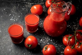 Jug with tomato juice on the table. On a black background. High quality photo. Jug with tomato juice on the table. 