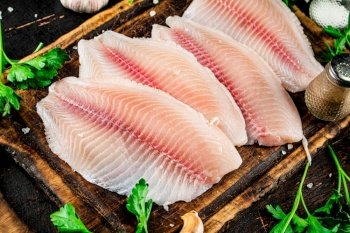 Raw fish fillet with greens on a cutting board. Against a dark background. High quality photo. Raw fish fillet with greens on a cutting board. 