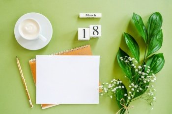 Wooden cubes calendar March 18. Notepad, cup of coffee, bouquet flowers on green background. Concept hello spring Creative Top view Flat lay Mock up.. Wooden cubes calendar March 18. Notepad, cup of coffee, bouquet flowers on green background. Concept hello spring Top view Flat lay Mock up