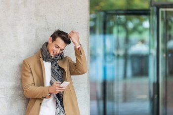 Cheerful man leaning against wall in the city using smartphone