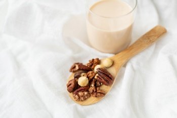 Vegan milk from nuts in a glass cup with various nuts on a white table, nuts in a wooden spoon. Vegan milk from nuts in a glass cup with various nuts on a white table, nuts in a wooden spoon.