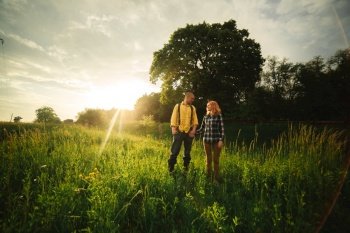 Loving hipster couple walking in the field, kissing and holding hands, hugging, lying in the grass in the summer at sunset. valentines day.. Loving hipster couple walking in the field, kissing and holding hands, hugging, lying in the grass in the summer at sunset. valentines day