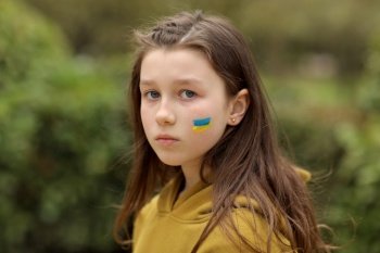 the face of a frightened girl, painted on her cheek in the yellow-blue colors of the Ukrainian flag, a request for help. Children ask for peace. High quality photo. High quality photo.. the face of a frightened girl, painted on her cheek in the yellow-blue colors of the Ukrainian flag, a request for help. Children ask for peace. High quality photo. High quality photo