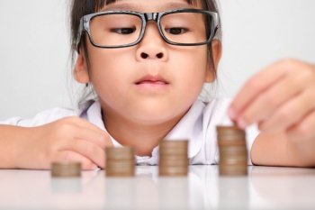 Cute asian little girl making stacks of coins. Little kids save money for future education.