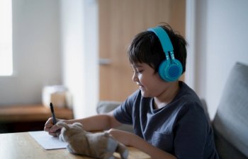 A happy kid wearing some headphones and listening to music while drawing on paper, Indoor portrait by Cute boy enjoy a creative activity at home on a weekend. A Child is doing homework