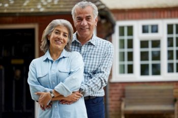 Portrait Of Mature Couple Standing In Garden In Front Of Dream Home In Countryside    