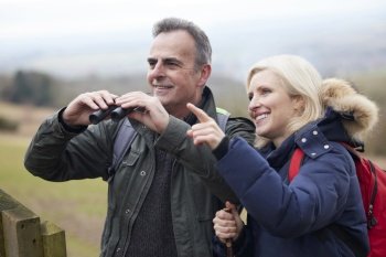 Mature Couple On Walk In Winter Countryside Looking At Wildlife Through Binoculars