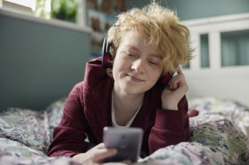 Teenage Girl Wearing Wireless Headphones Listening To Music Steaming From Mobile Phone At Home 
