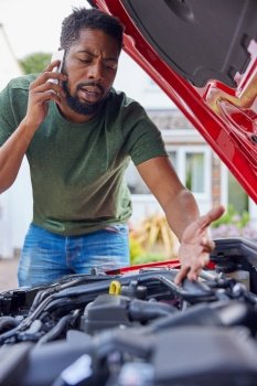 Man Looking At Engine After Car Breakdown Calling Auto Recovery On Mobile Phone