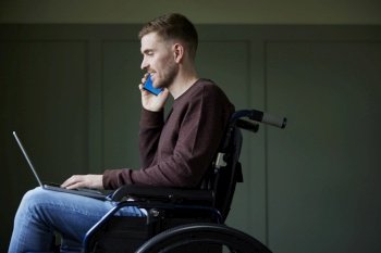 Man in Wheelchair Working From Home Using Laptop And Mobile Phone