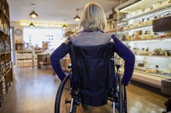 Rear View Of Woman In Wheelchair Shopping For Food In Delicatessen