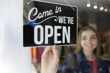 Smiling Female Owner Of Small Business Turning Round Open Sign In Shop Window