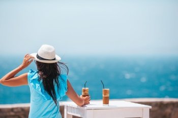 Young woman drinking cold coffee enjoying sea view in outdoor cafe. Young woman drinking cold coffee enjoying sea view