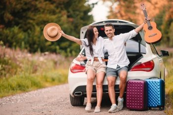 Young couple travelers sitting in trunk of a car on summer car vacation. Young couple tourist enjoying on summer vacation