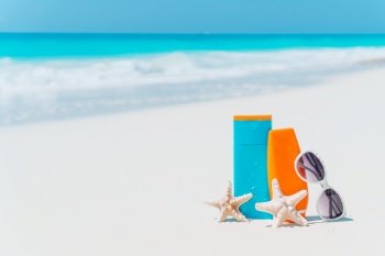 Suncream bottles, goggles, starfish and sunglasses on white sand beach background ocean. Suncream bottles, sunglasses, starfish on white sandy beach