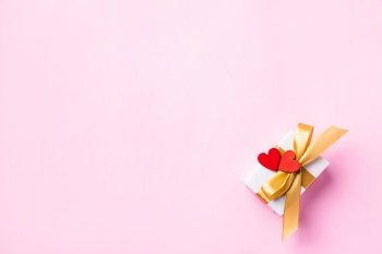 Valentines’ day background concept. White gift box with a golden bow ribbon and wood red hearts composition greeting card for happy love isolated on pink background with copy space. View from above