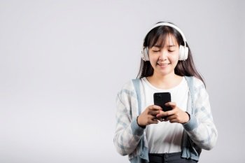 Woman excited smiling listening to music radio in bluetooth headphones and holding phone studio shot isolated white background, happy Asian young female listen modern technology mobile phone