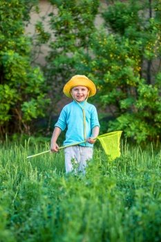 A charming kid playing with a scoop on a meadow in a warm and sunny summer or spring day. Active rest for children. A boy boy is fun with pleasure for butterflies and mistakes.. A charming kid playing with a scoop on a meadow in a warm and sunny summer or spring day.