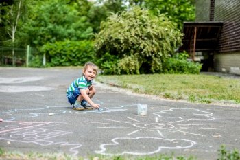 Cute boy and girl drawing with chalk on the sidewalk in the park. Summer activities for children. Creative drawing of a child with blue chalk on the road.. Cute boy and girl drawing with chalk on the sidewalk in the park.