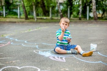 Cute boy and girl drawing with chalk on the sidewalk in the park. Summer activities for children. Creative drawing of a child with blue chalk on the road.. Cute boy and girl drawing with chalk on the sidewalk in the park.