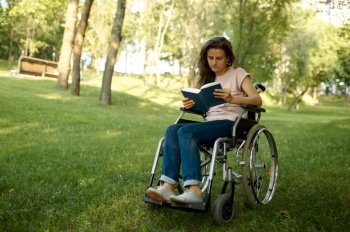 Disabled woman in wheelchair reading a book in park. Paralyzed people and disability, handicap overcoming. Handicapped female person leisures outdoors. Disabled woman in wheelchair reading book in park