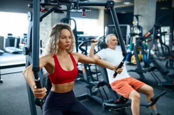 Old man and female personal trainer on exercise machines, gym interior on background. Sportive grandpa with woman instructor, training in sport center. Healty lifestyle, health care. Old man and female trainer on exercise machines