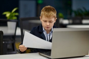 Portrait of little handsome businessman working with paper contract document and laptop in office. Little handsome businessman working in office portrait