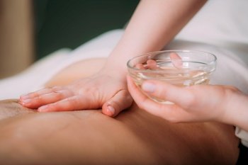 Massaging with massage oil, hands of a female massage therapist massaging a female client