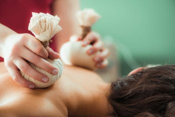 Kizhi massage or herbal bolus bags Ayurveda massage, hands of an Ayurveda Massage therapist pressing herbal bolus bags onto client’s skin