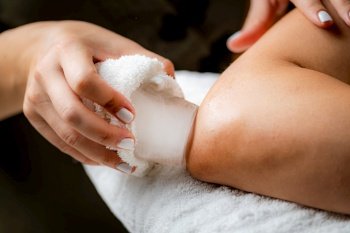 Ice Massage for Painful Elbow. Hands of a therapist placing ice directly onto a painful elbow to relieve pain, reduce inflammation and swelling and promote healing.. Ice Massage for Painful Elbow.