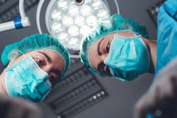 From below female surgeons in medical uniform using professional tools while standing under bright light in operating theater. High quality photo. From below female surgeons in medical uniform using professional tools while standing under bright light in operating theater