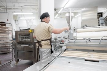 Baker working at industrial bakery preparing trays with fresh loaf. High quality photo. Baker working at industrial bakery preparing trays with fresh loaf. 